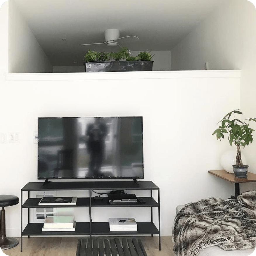 Slim media console with black metal frame styled with books and electronics below a TV in a living room.