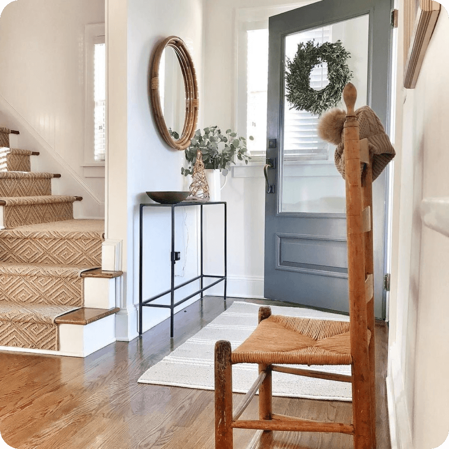 Slim console table with black metal frame styled with decor beneath a mirror near an entry door and stairs.