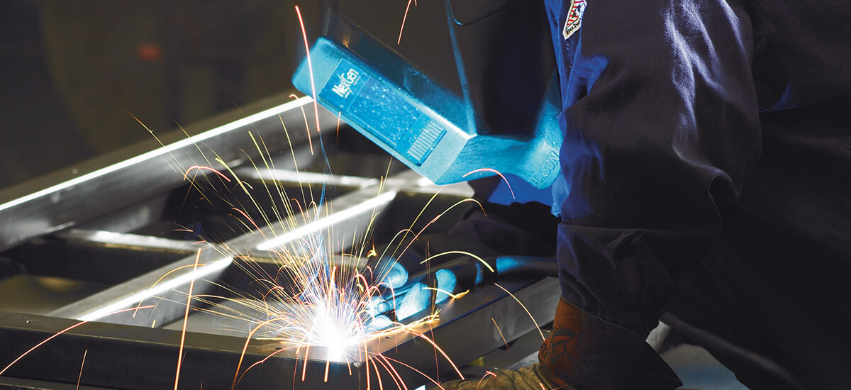 Person using a welding torch on a metal frame with sparks in a workshop environment.
