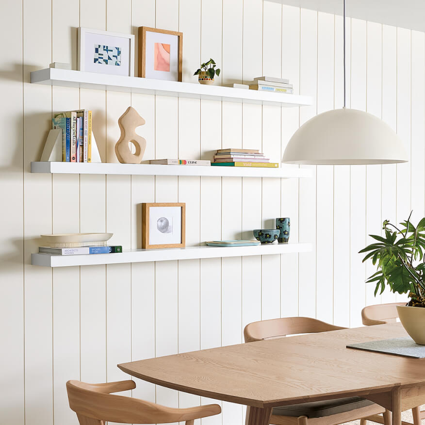 Float shelves in white mounted on paneled wall, styled with books, framed art, and decor above wood table.