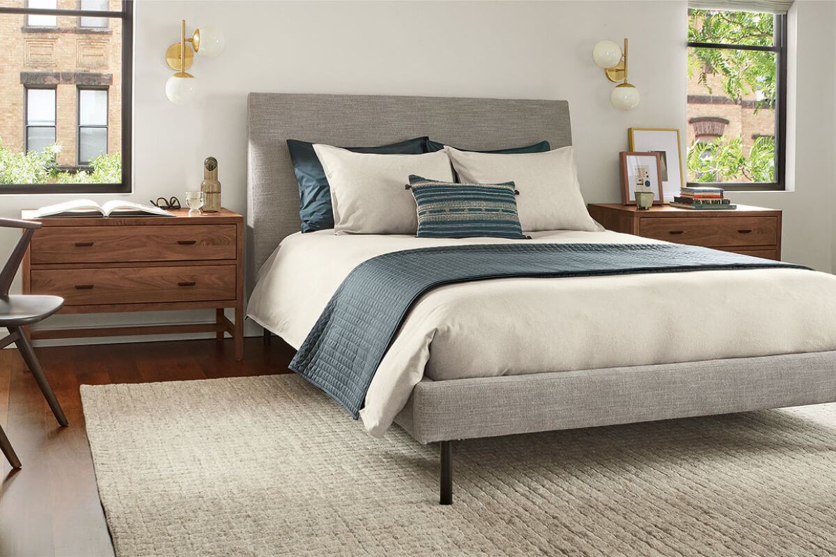 Ella bed with grey fabric frame and blue accent throw paired with Berkeley nightstands and wall sconces.