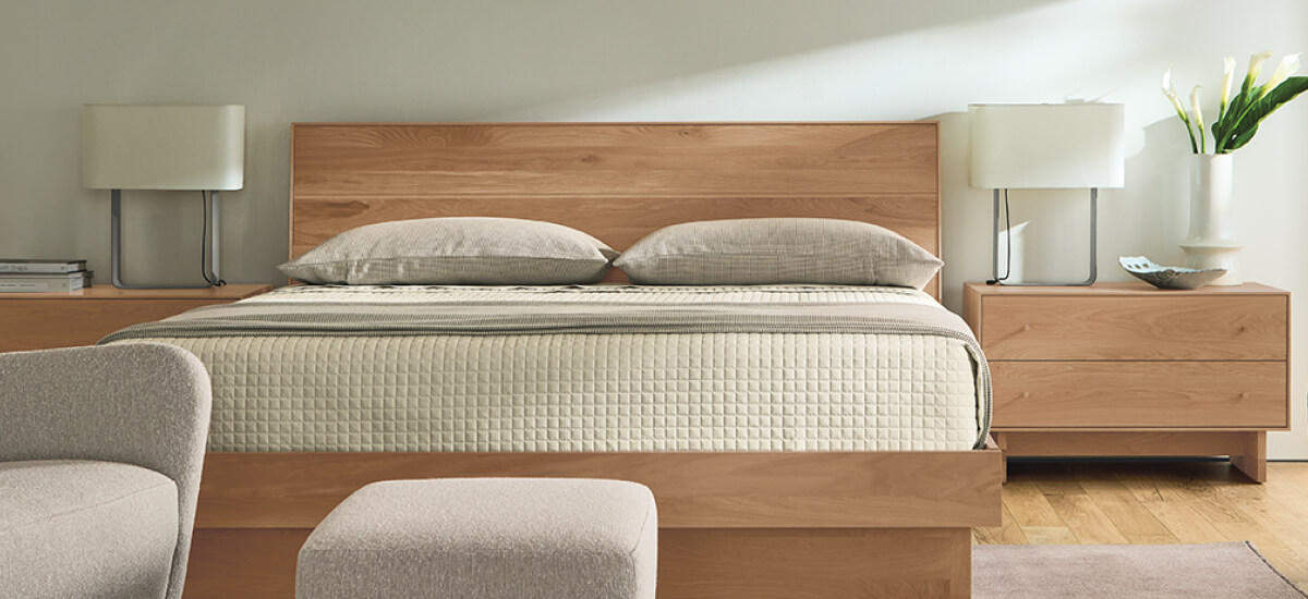 Bedroom with wood bed and nightstands, neutral quilted bedding, table lamps, and upholstered seating.