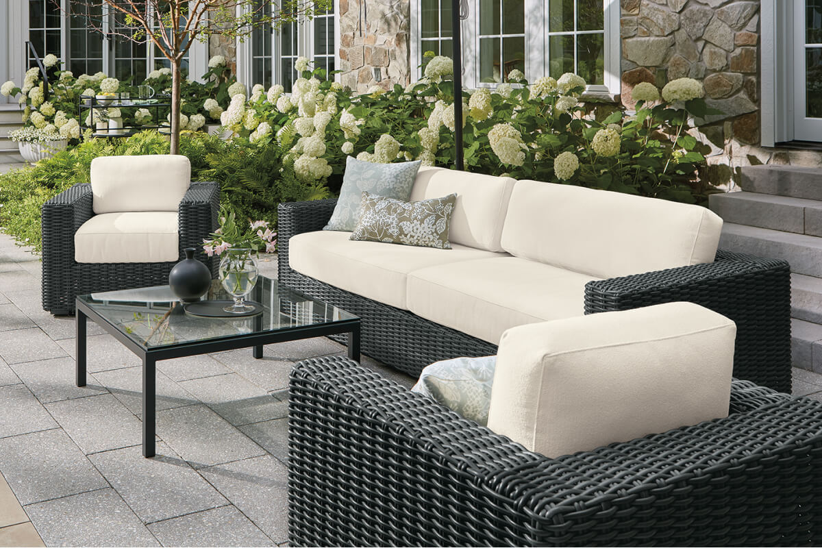 Madura seating with a cream sofa and two chairs in dark grey wicker on a patio with a glass coffee table.