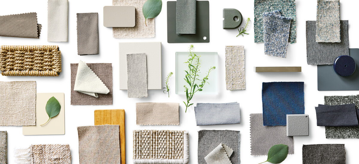 Assorted fabric swatches, wood samples and material finishes arranged on a neutral background with greenery accents.