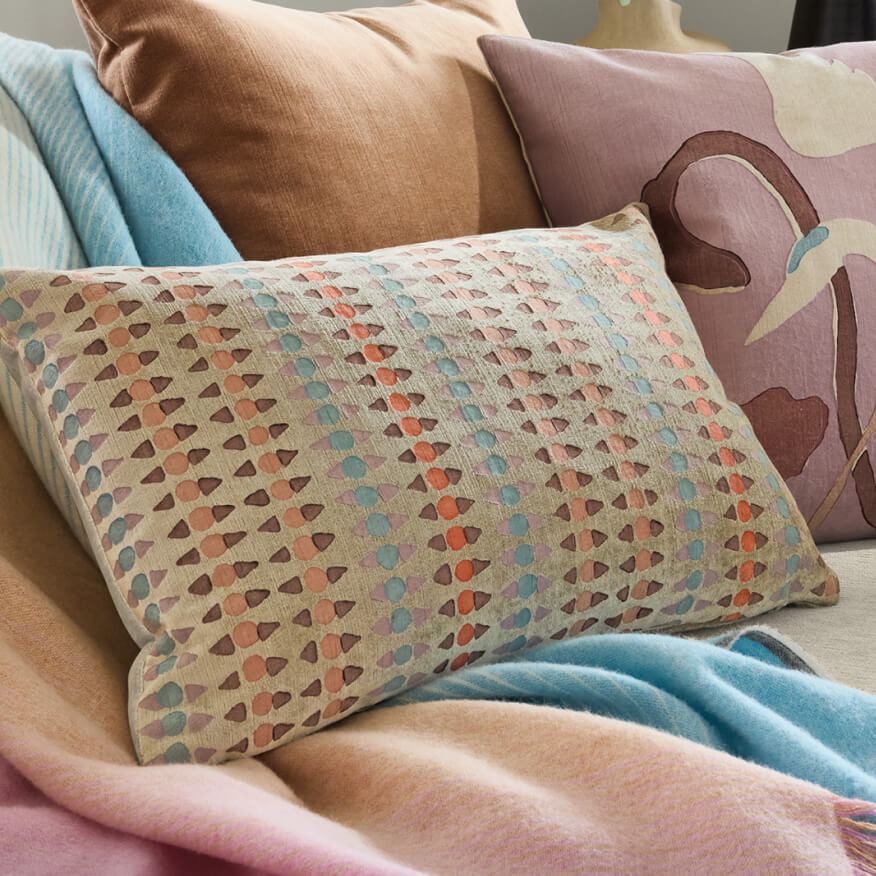 Stockholm pillow with multicolor geometric pattern, layered with solid pillows and a throw blanket on a sofa.