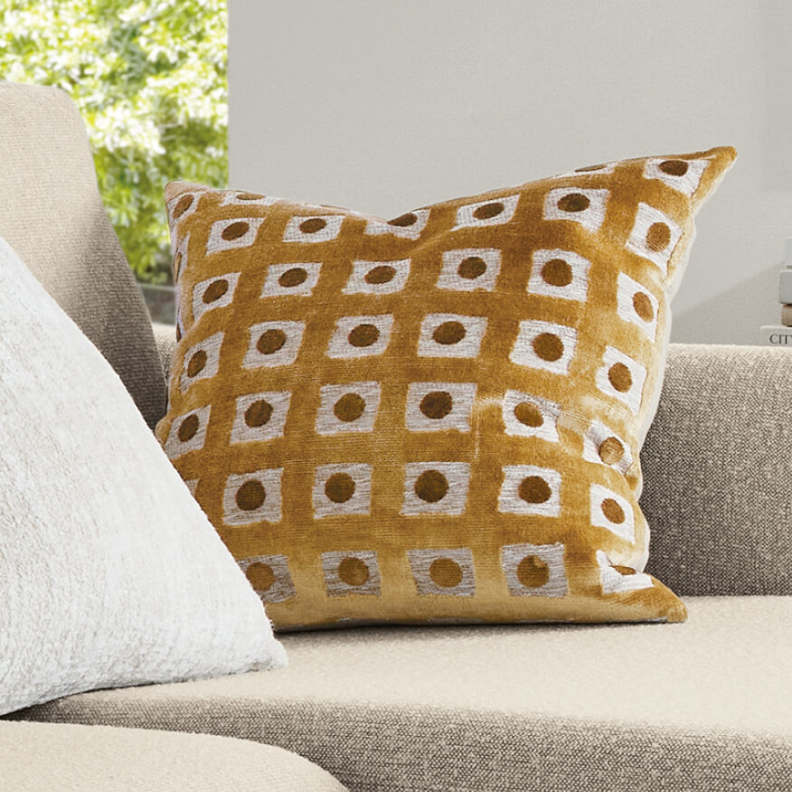 Ellsworth pillow in mustard with a white geometric pattern, set on a neutral sofa beside a light pillow.