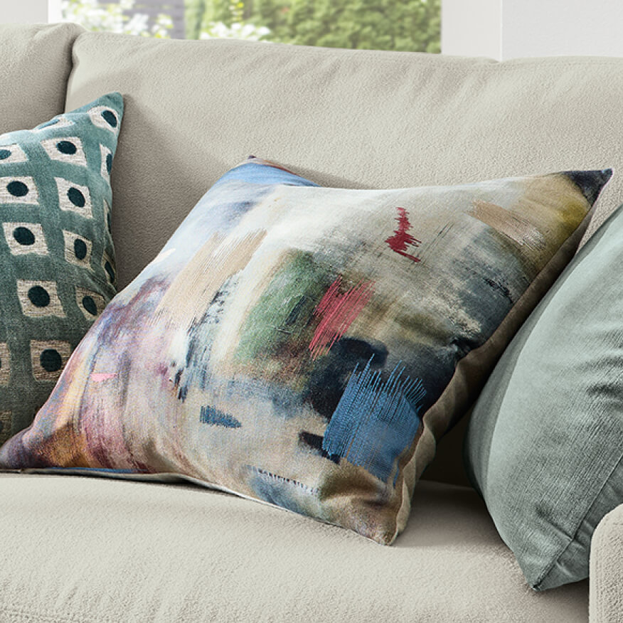 Abstract Tiden pillow in multicolor tones, styled on a neutral sofa with teal pillows.