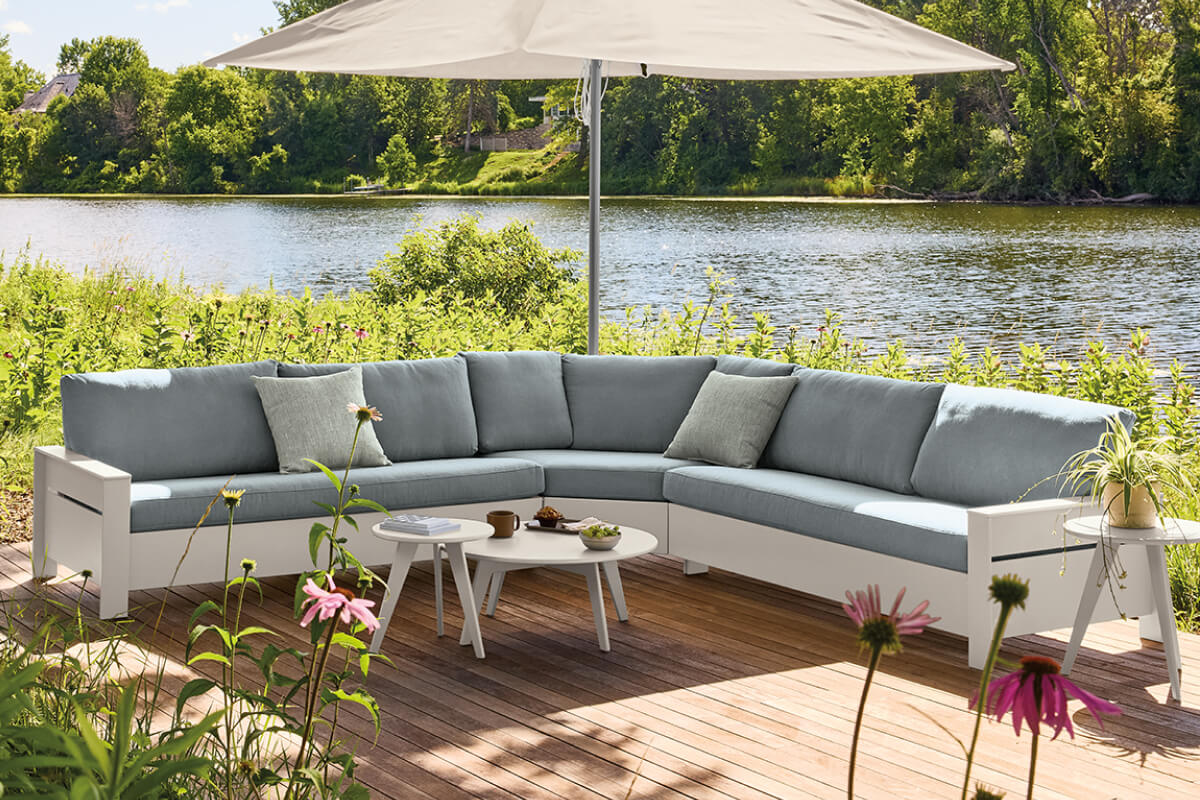 Rayo sectional in light blue with a white frame, set with Nova tables on a deck overlooking a lake.