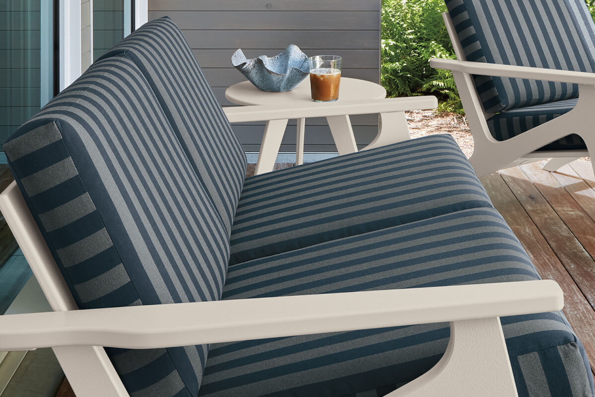 Breeze seating with blue striped cushions and white frame, paired with a round side table on a deck.