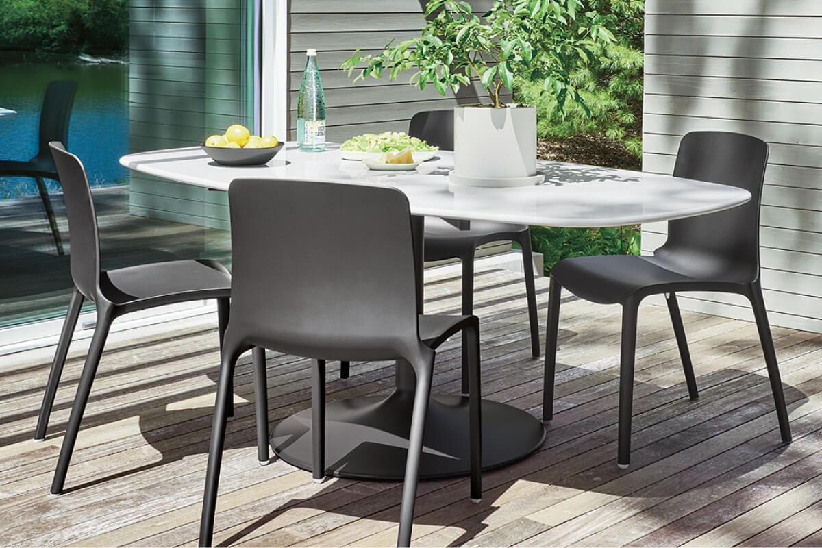Aria boat top dining table with four black Tiffany chairs, styled with lemons, bottle, and planter on a deck.