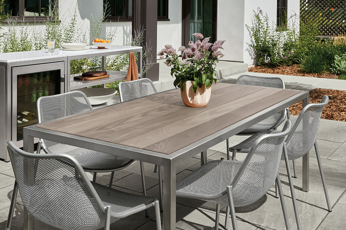 Montego table with wood top and metal frame, paired with Soleil chairs and a modern outdoor kitchen.
