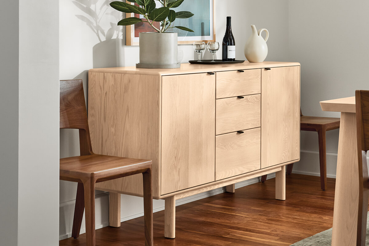 Hensley storage cabinet in light wood with doors and drawers, styled with a plant, wine, and glassware.