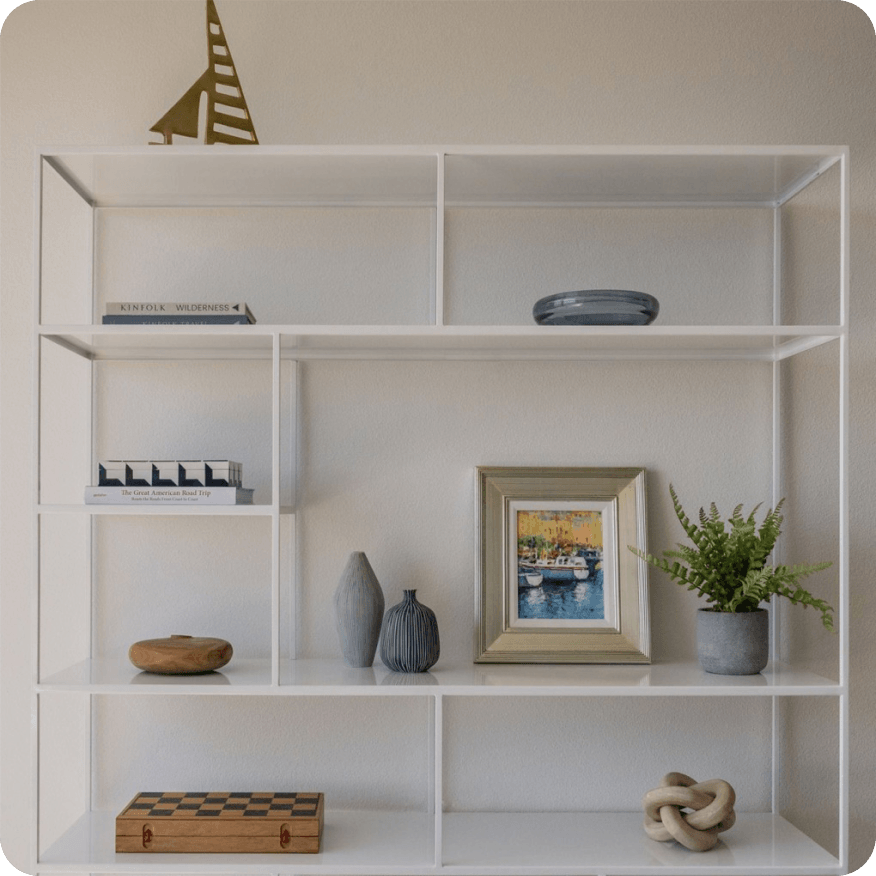 White Foshay bookcase with open shelves holding books, framed art and small decor objects.