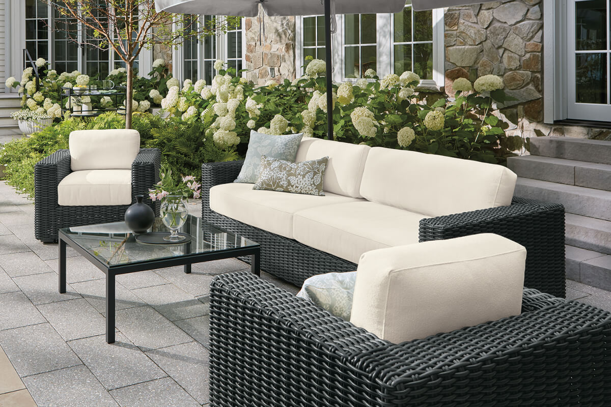 Madura outdoor sofa and chairs with woven black frames and cream cushions around a glass coffee table.