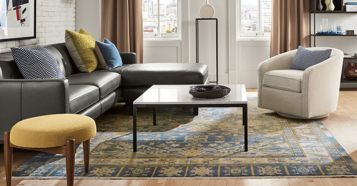 Kayseri rug with blue and gold patterned border beneath a black leather sectional, swivel chair and coffee table.