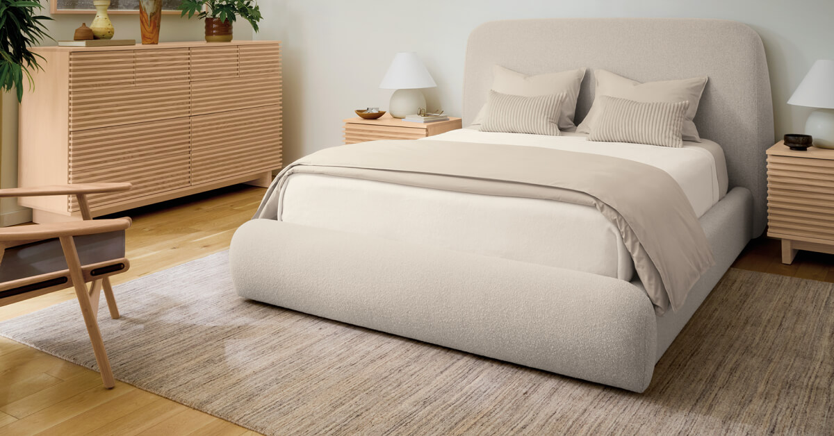 Nomad rug in soft neutral tones beneath an upholstered bed, wood nightstands and matching dresser.