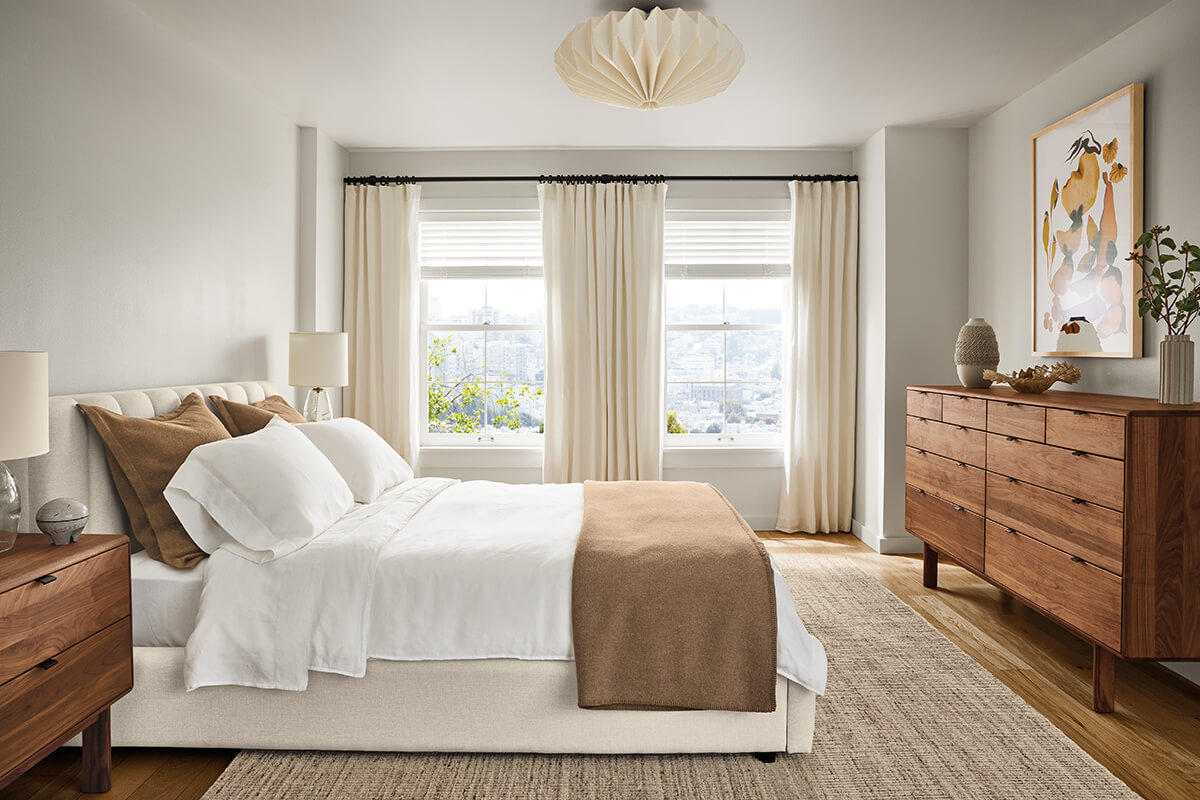 Hartley bed with a channel-tufted headboard, white bedding and tan throw across from a walnut Hensley dresser.