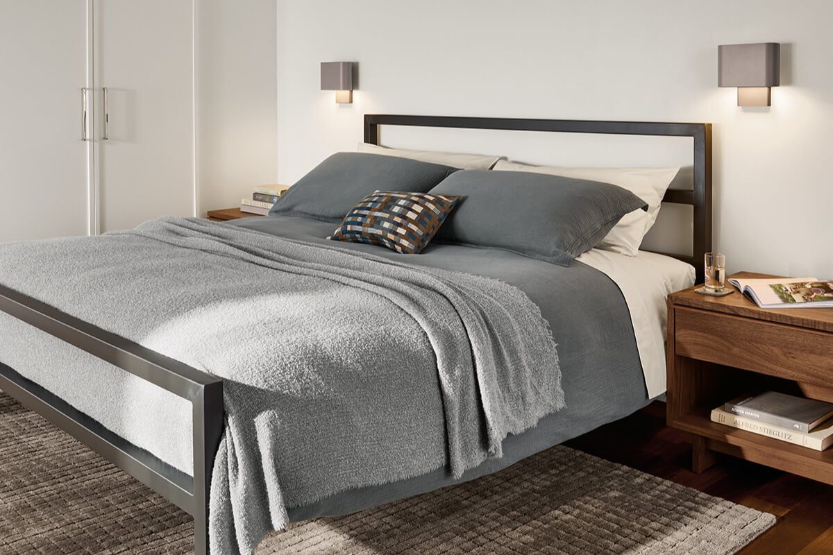 Parsons bed with a black metal frame, layered grey bedding and Kalli wall sconces mounted above nightstands.