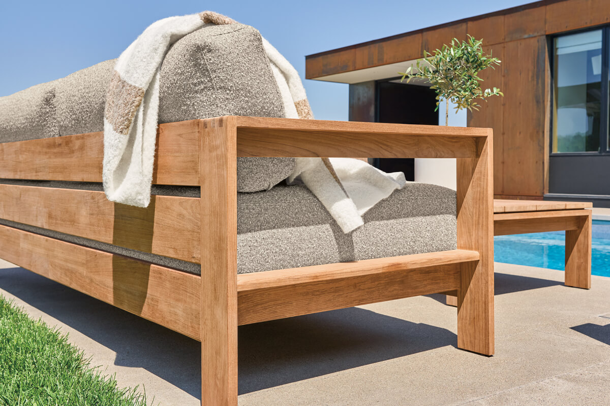 Leti outdoor sofa with slatted teak frame, textured upholstery and neutral throw blanket by the pool.
