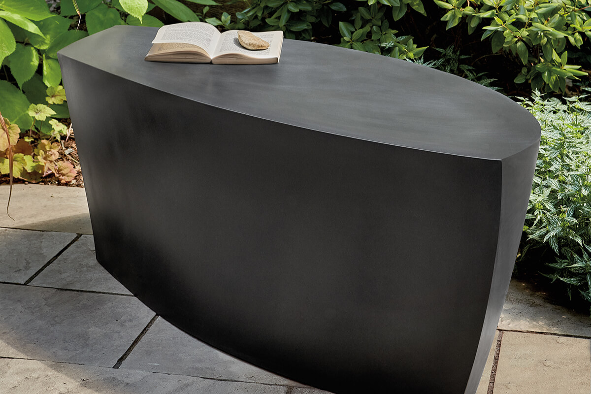 Gehry outdoor table with sculptural black finish and rounded silhouette, styled with an open book in a garden.