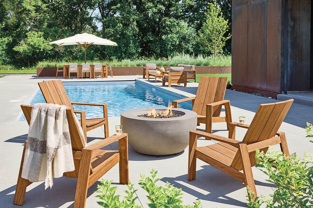 Timor outdoor chairs in solid teak arranged around a fire table beside a pool.