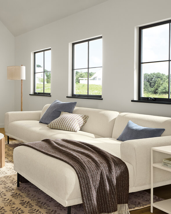 Ali sectional in ivory upholstery with blue accent pillows and a gray throw draped across the chaise.