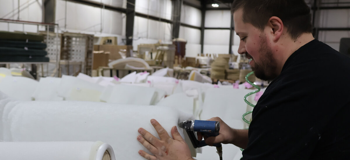 Upholstery craftsperson preparing foam cushion pieces by hand in a furniture workshop.
