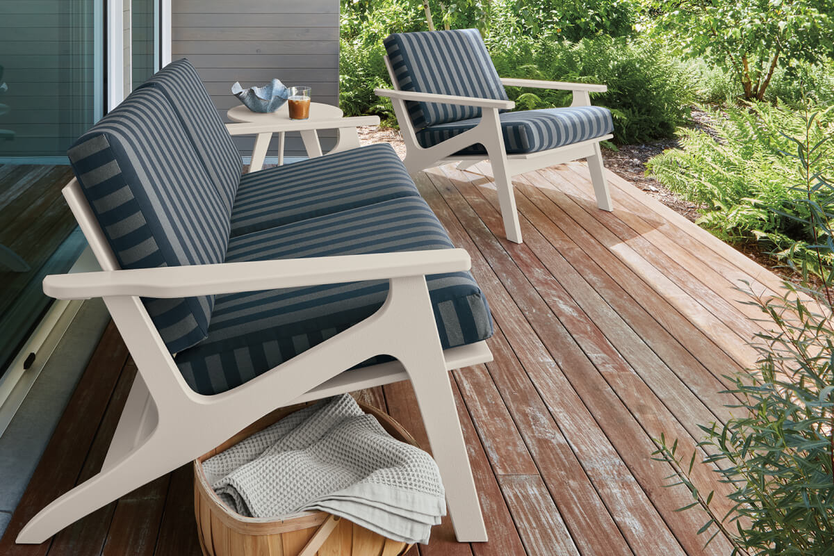 Breeze outdoor sofa and lounge chair with blue striped cushions on a wood deck overlooking lush garden landscaping.