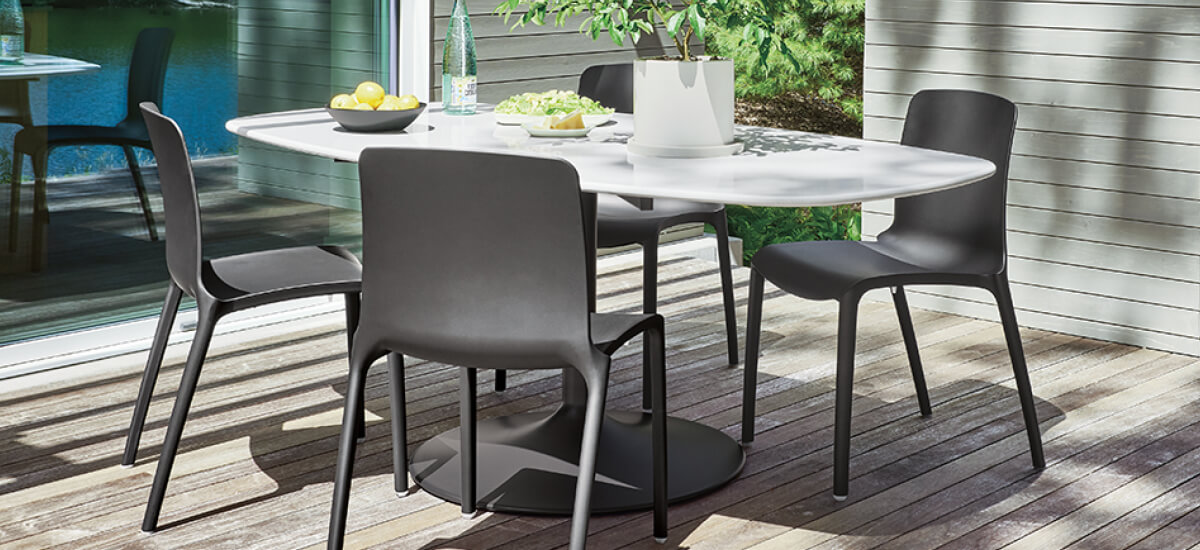 White Aria outdoor boat top dining table with four black dining chairs, topped with a planter, lemons, glass bottle, and serving bowls.
