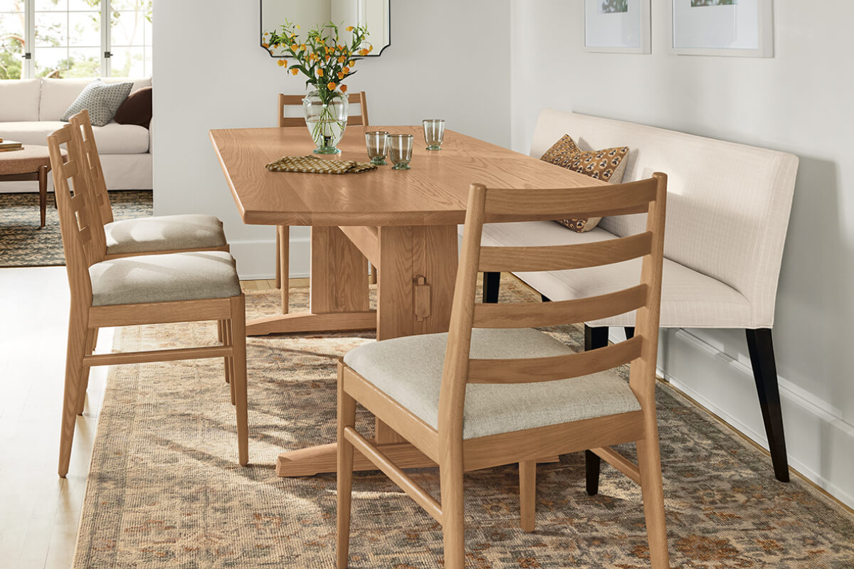 Salem dining table paired with an Ava banquette and Conway chairs in oak, styled with glassware and a vase of flowers.