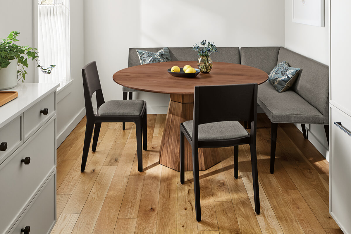 Glover dining table with an Ava corner banquette, upholstered chairs, and a walnut top styled with flowers and fruit.