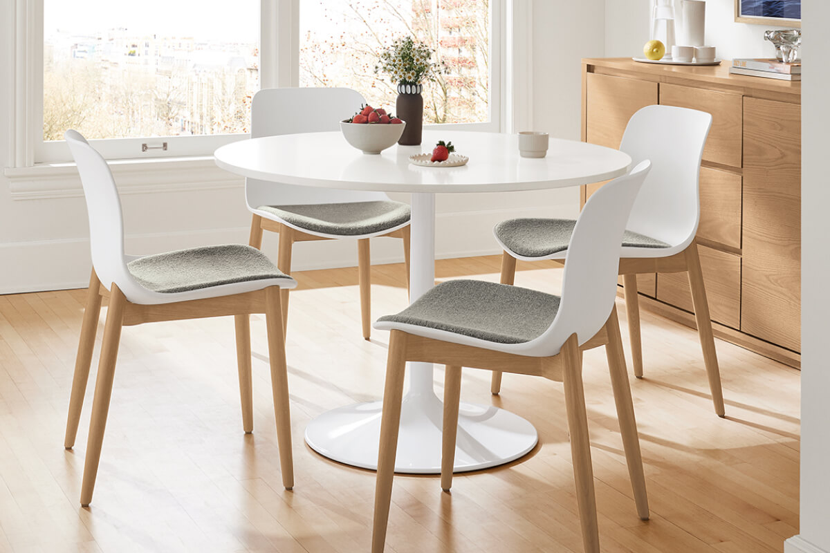 White Aria dining table with a pedestal base and four Pasqual chairs featuring upholstered seats and wood legs.