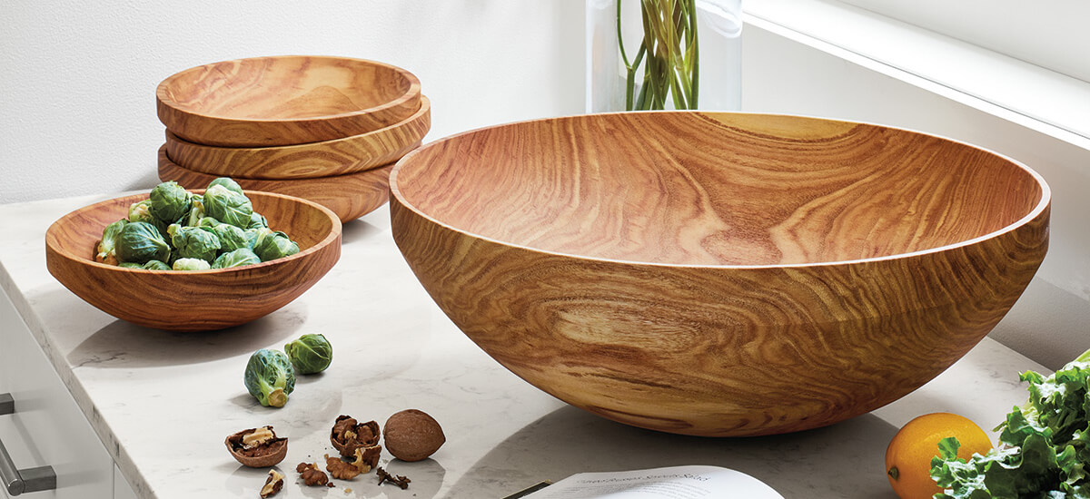 Various wood bowls on a white counter with vegetables.