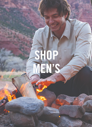 Smiling man warming his hands over a fire with mountains in background