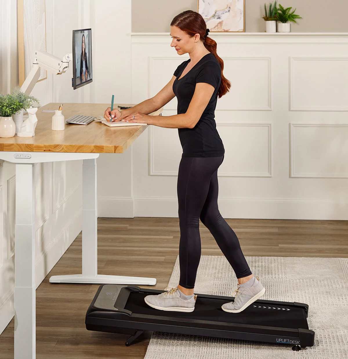 A woman walking on an UPLIFT Desk Inclining Walking Pad while working at her standing desk