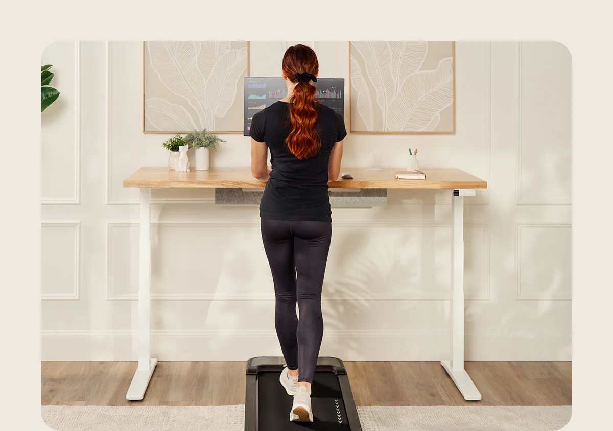 A woman using an UPLIFT Inclining Walking Pad at her desk
