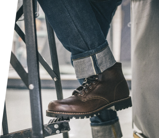 Image focusing on a brown leather boot below a cuffed jean pant leg, the wearer stepping on the bottom rung of a steel ladder.
