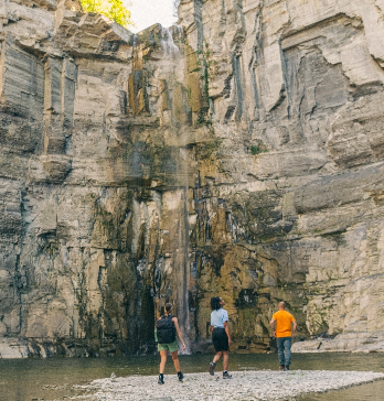 3 people stand before a rocky wall with a slight waterfall