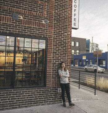 A man leaning against the outside brick wall of a town coffee shop