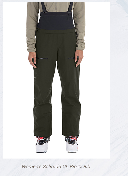 Woman wearing green bib pants, black suspenders, and ski boots. Text below reads Womens Solitude UL Bio 1/4 Bib.