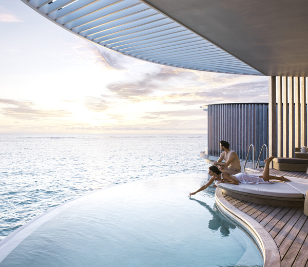 Couple in luxurious suite with private pool and view of the ocean. The woman is lying down, dipping her hand in the water.