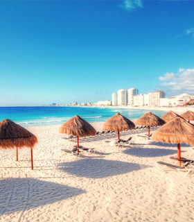 View of a beach in Cancun with natural, thatched umbrellas.