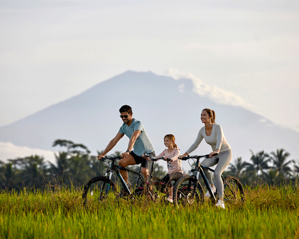 A family of three is bicycling through a grassy field.
