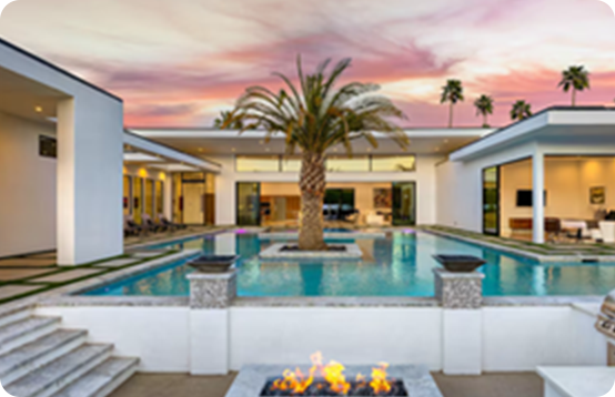 Luxury villa with a central palm tree, pool, and firepit at sunset under pink-orange skies.