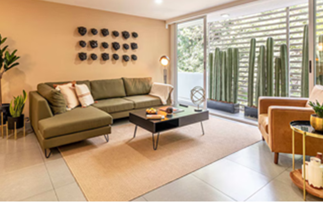 Bright living room with green sectional sofa, wall art, and large windows overlooking tall outdoor cacti.