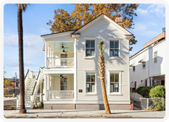Classic white two-story home with double porches and palm tree in front.