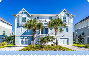 Large coastal-style home with light-blue siding, palm trees, and a bright, sunny backdrop.