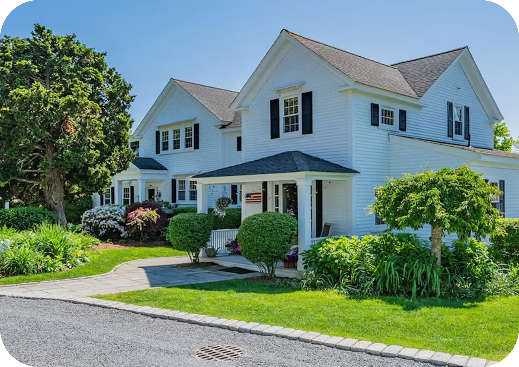 Two‑story white house with a front porch, green lawn, and garden landscaping.