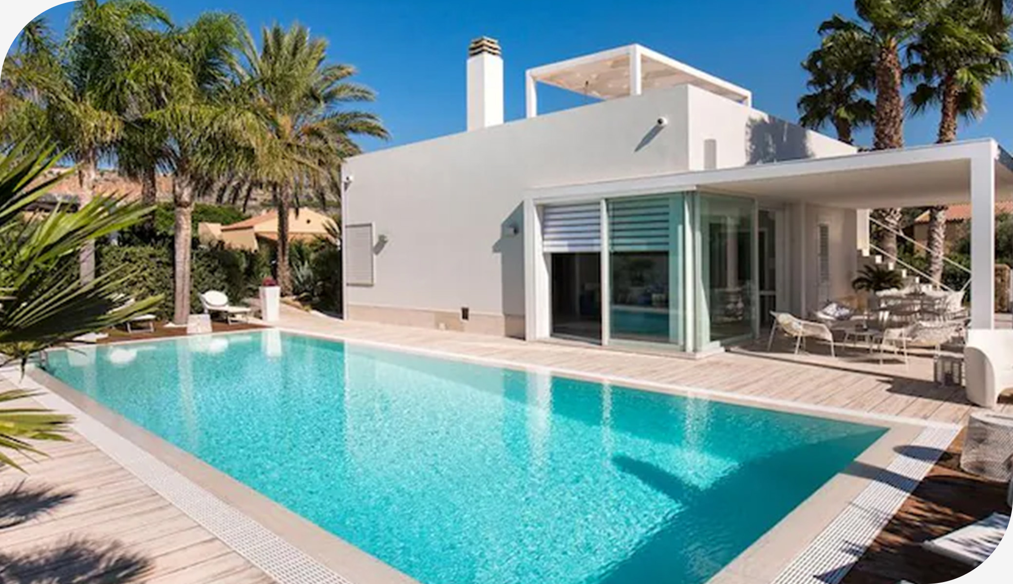 Bright modern villa with palm trees and a long pool set under a clear blue sky in Sicily.