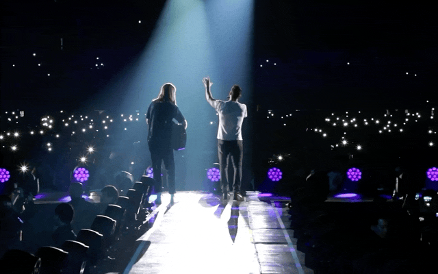 Animated gif of a video showing a concert with lights, a crowd cheering, and a person playing guitar.